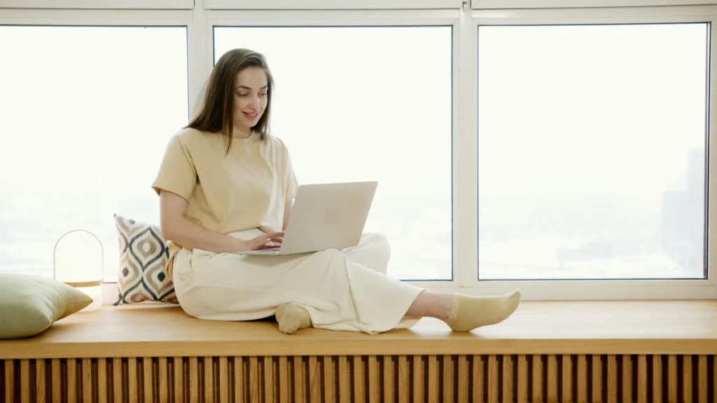 woman sitting by window working on laptop